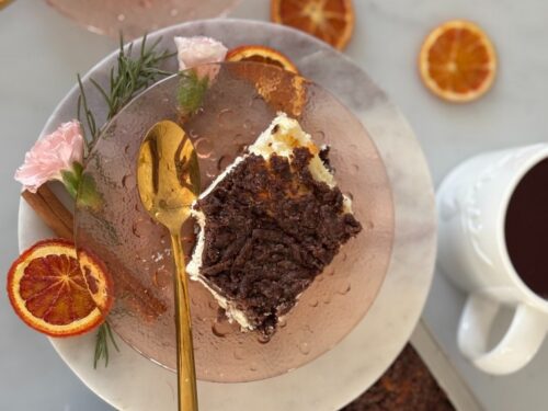 Sernik królewski podany na talerzu wokół którego leżą kawałki pomarańczy